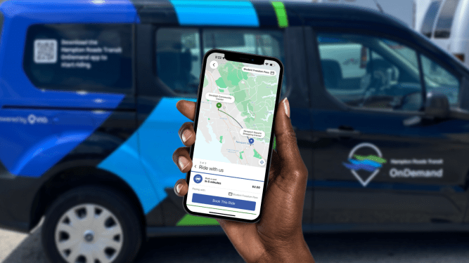 hand holding smartphone with transit app open. minivan in the background with via logo