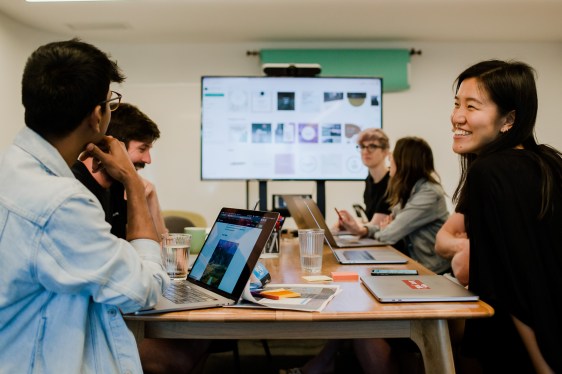 Students sitting around a table, laptops open, large monitor at one end