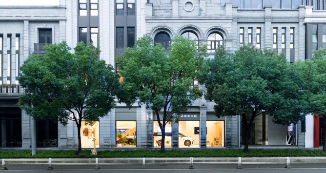 Building facade with trees blocking the view of a Zeekr vehicle in a storefront window
