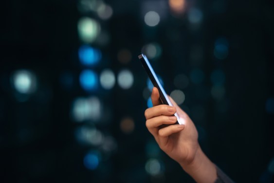 Close up shot of female hand using smartphone at night, against illuminated and defocused bokeh in background.