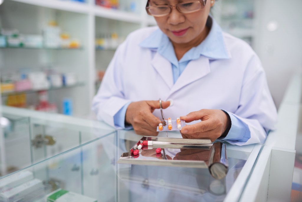 Pharmacist cutting medication package for the customer, used in post about Medigo app