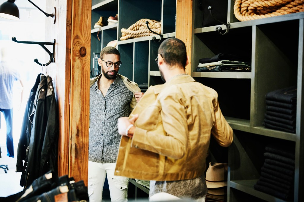 Man trying on jacket while looking in the mirror in men's clothing shop