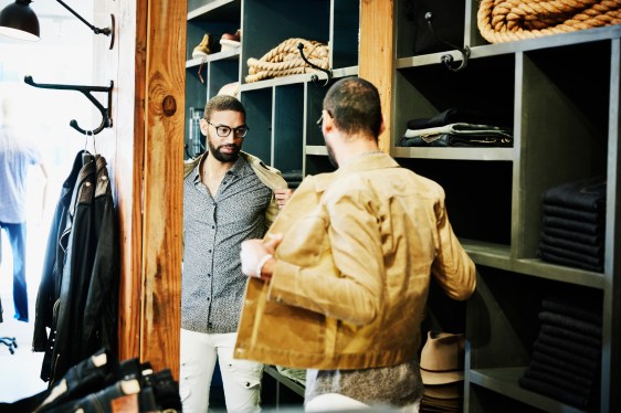 Man trying on jacket while looking in the mirror in men's clothing shop
