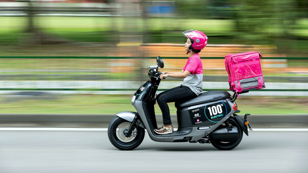woman in side view riding gogoro electric scooter with delivery parcel on back