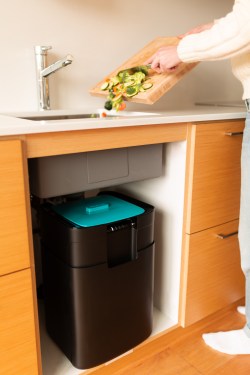 scraping vegetables off a cutting board into a sink, with a Sepura composter underneath
