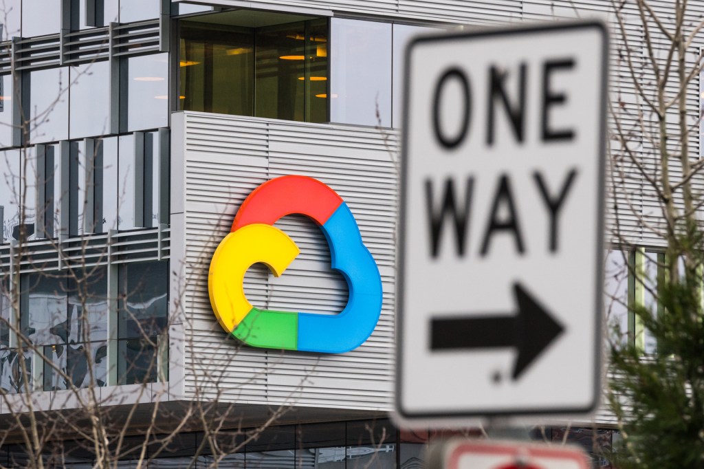 Google Cloud symbol on a building with a One Way sign in the forefront of the picture.