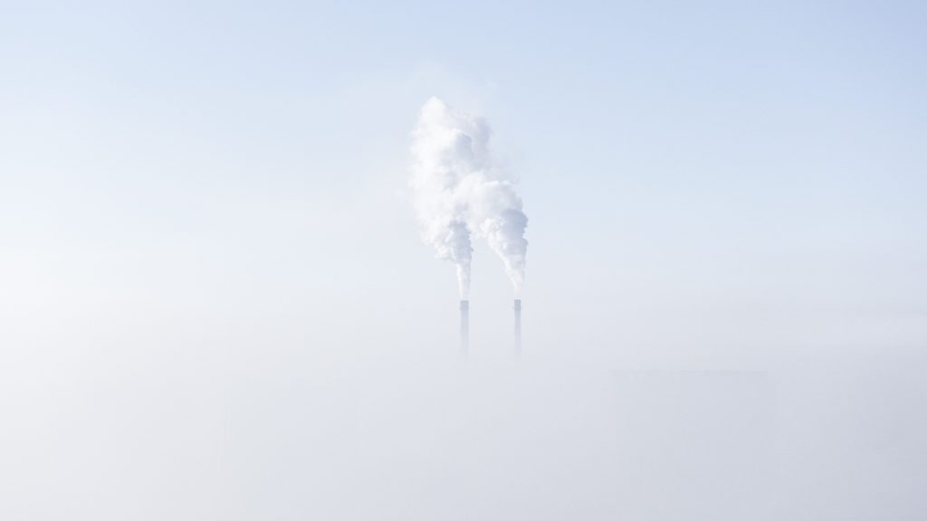 Smoke stacks emit pollution above a layer of fog.