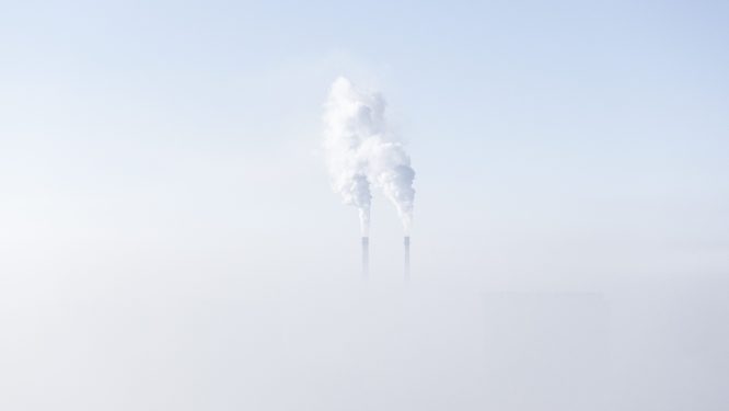 Smoke stacks emit pollution above a layer of fog.