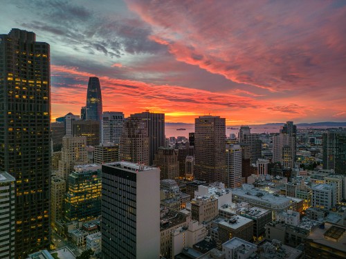Aerial view over San Francisco with a burning sunrise over the Bay. Skyscrapers fill the skyline.