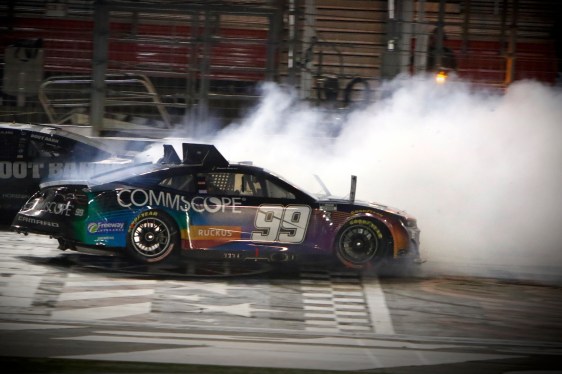 a NASCAR vehicle with the hood billowing with smoke, with the car featuring the CommScope's corporate branding