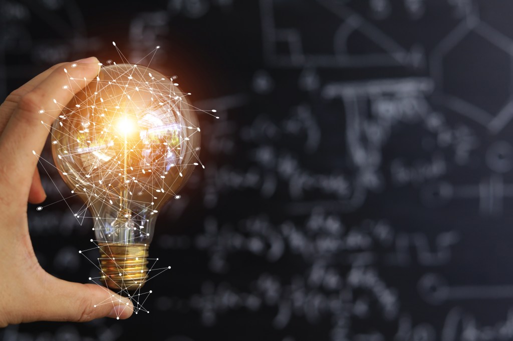 Light bulb in a person's hand in front of a blackboard with equations written on it.