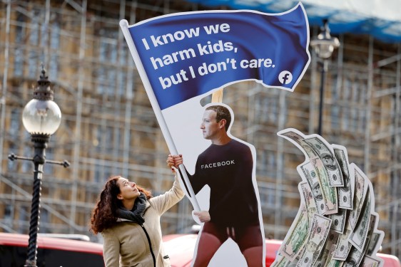A demonstrator poses with an installation depicting Facebook founder Mark Zuckerberg surfing on a wave of cash and surrounded by distressed teenagers