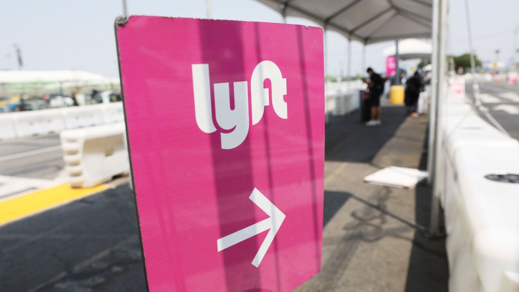 Air travelers wait in the ride share lot near a sign for Lyft at Los Angeles International Airport (LAX).