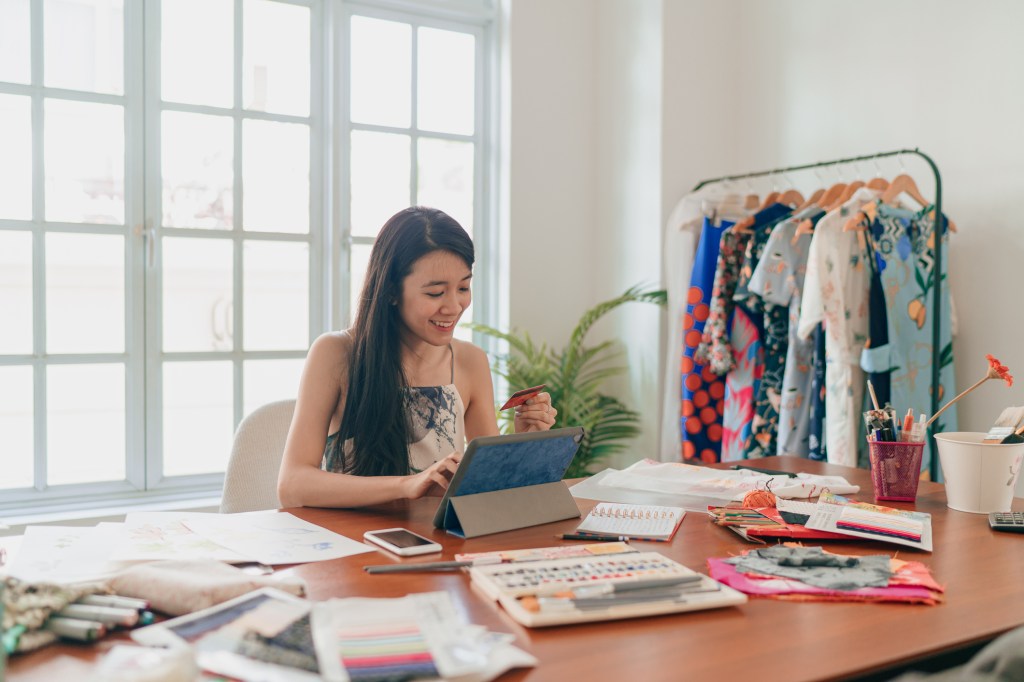 Woman on laptop in workplace filled with clothes, used in post about Jenfi