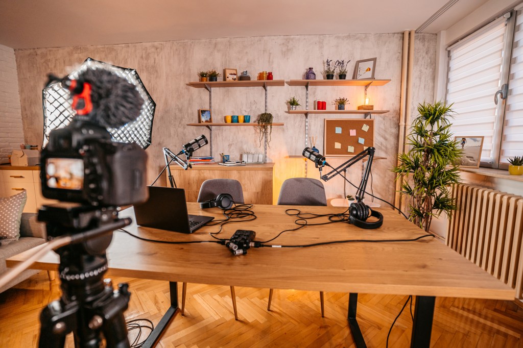 Office prepared for recording a broadcast with camera and microphones on a large wooden table.