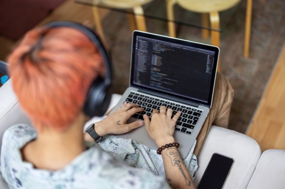 Over the shoulder view of a man coding on his laptop while sitting.