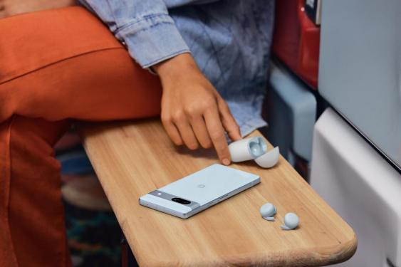 Google Pixel 7a and ear buds on bench next to a person