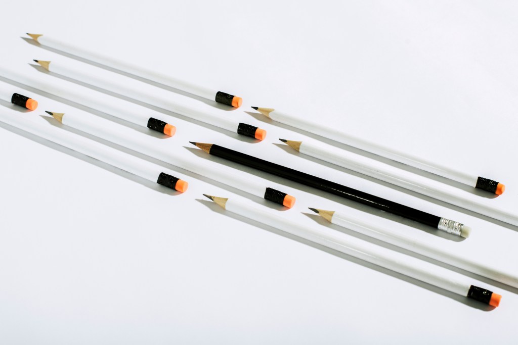 Row of white pencils and one black pencil, lying on a white background