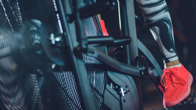 Lower section of unrecognizable female's athlete feet pedaling on a stationary air bike at the gym.