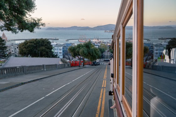 A view from a vintage San Francisco cable car travelling down Hyde Street, overlooking the San Francisco Bay at sunset.