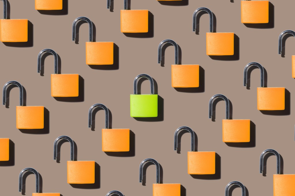 A Locked Green Colored Padlock Standing out from Opened Orange Colored Padlocks on Brown Background Directly above View, used in a post about Notarize and Proof