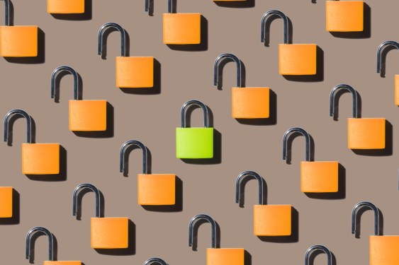 A Locked Green Colored Padlock Standing out from Opened Orange Colored Padlocks on Brown Background Directly above View, used in a post about Notarize and Proof