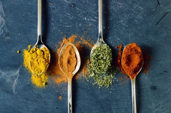 four spoons heaping with different spices against a gray background
