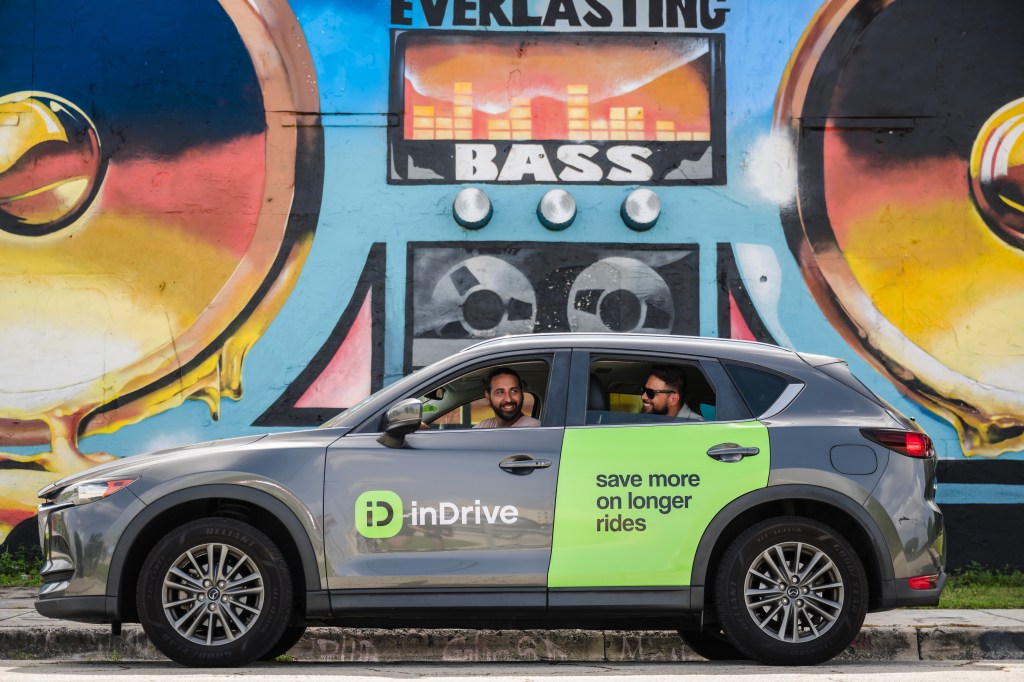 car with indrive logo, driver in front seat, rider in the back, in front of street art