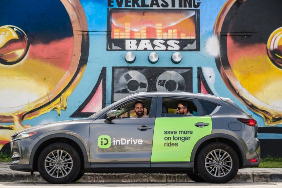 car with indrive logo, driver in front seat, rider in the back, in front of street art