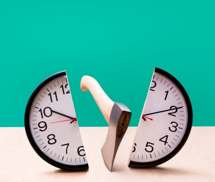 Analog wall clock being split in half by an axe, wood surface, green studio background