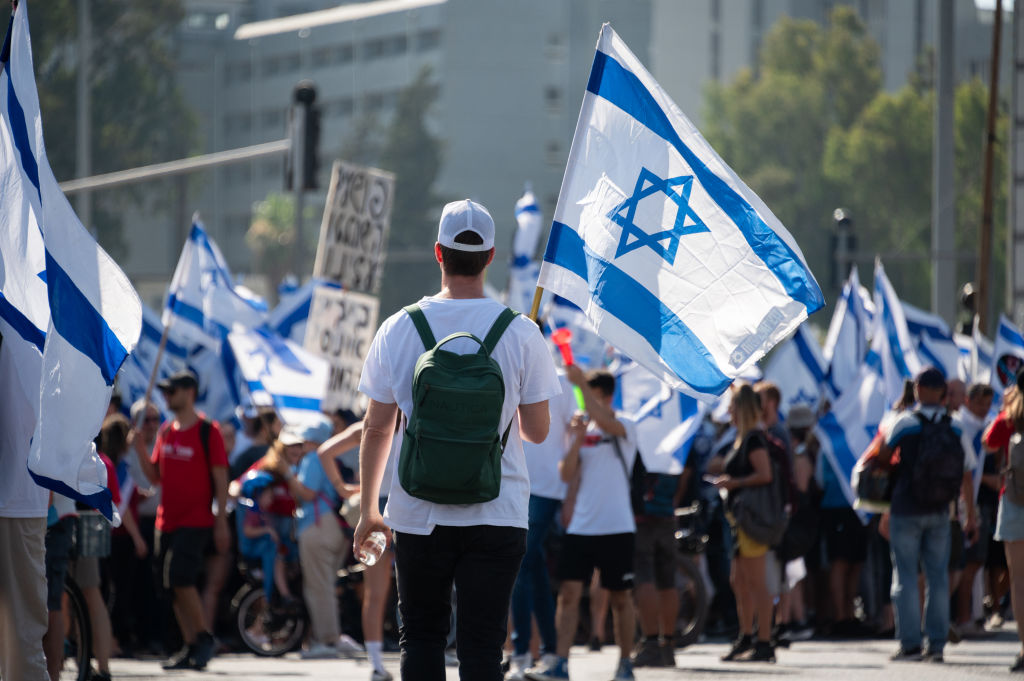 TEL AVIV, ISRAEL - JULY 18: A protester holds an Israeli flag during a demonstration outside HaShalom train station against the Israeli government’s judicial reform bill on July 18, 2023 in Tel Aviv, Israel. Netanyahu's government has been advancing controversial legislation to overhaul the country's Supreme Court, sparking a wave of demonstrations (Photo by Noam Galai/Getty Images)