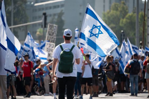 TEL AVIV, ISRAEL - JULY 18: A protester holds an Israeli flag during a demonstration outside HaShalom train station against the Israeli government’s judicial reform bill on July 18, 2023 in Tel Aviv, Israel. Netanyahu's government has been advancing controversial legislation to overhaul the country's Supreme Court, sparking a wave of demonstrations (Photo by Noam Galai/Getty Images)