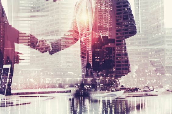 Two business men shaking hands over montage of a city scape photo.