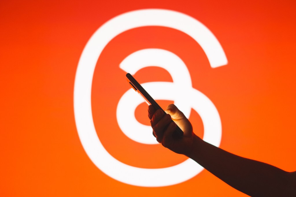 hand holding smartphone in front of Threads logo