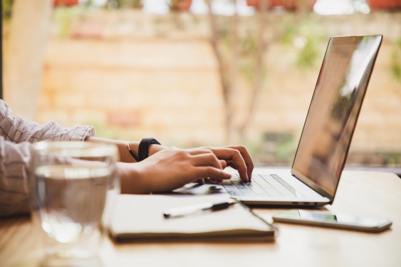 Hands of woman using a laptop, sitting at a wooden desk. Used in post about CakeResume.
