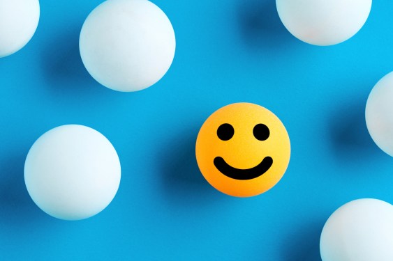 Smiling face emoticon or icon on a yellow ball surrounded by white balls on blue background.