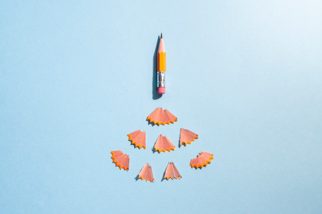 Worn orange pencil on a blue colored background with shavings arranged as if it's a rocket taking off