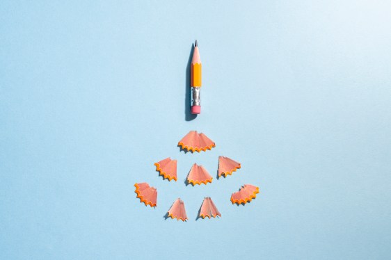 Worn orange pencil on a blue colored background with shavings arranged as if it's a rocket taking off