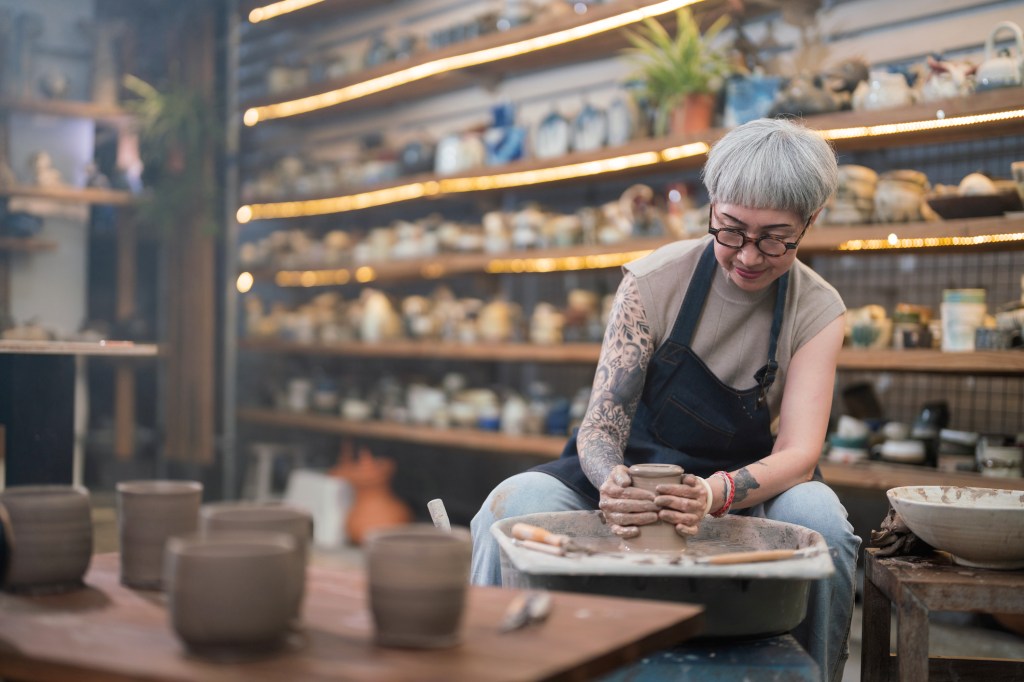 Senior woman artist making clay bowl on pottery wheel in pottery studio, used in post about Markato