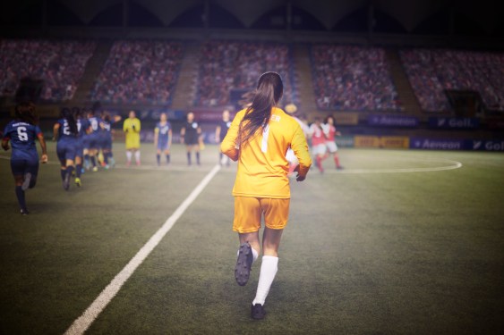 Determined female goalie jogs onto the field with her soccer teammates and alongside the opposing team for the pregame ceremony