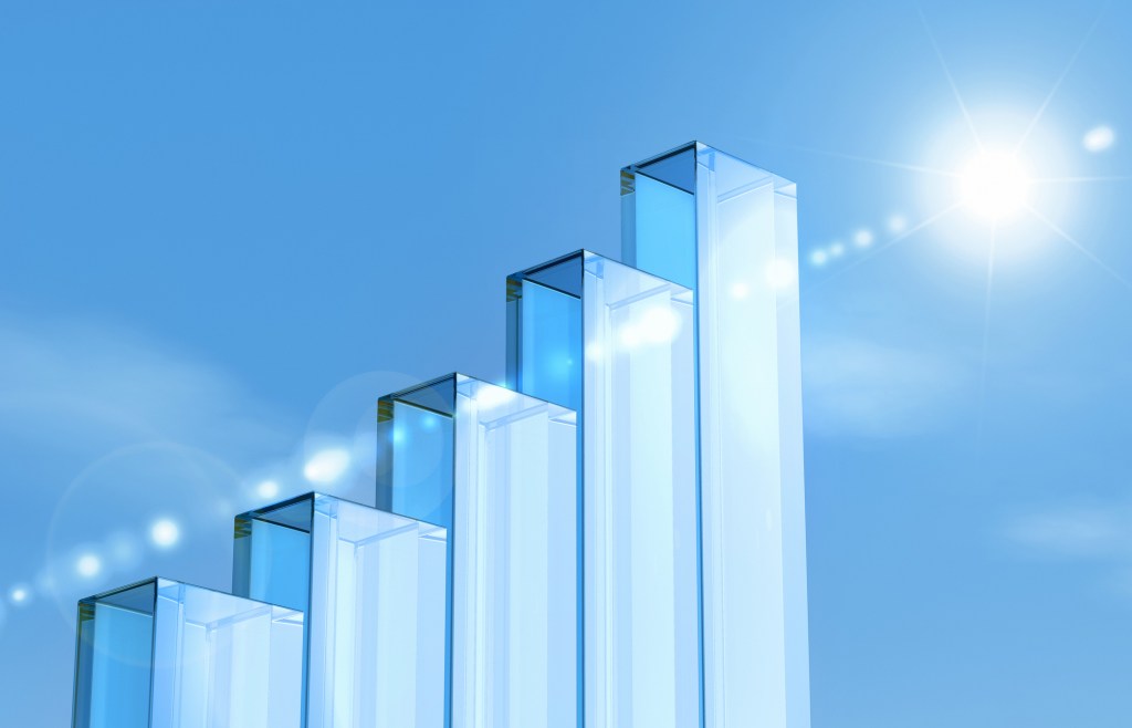 Glass pillars forming a growth bar graph against a bright blue sky background.