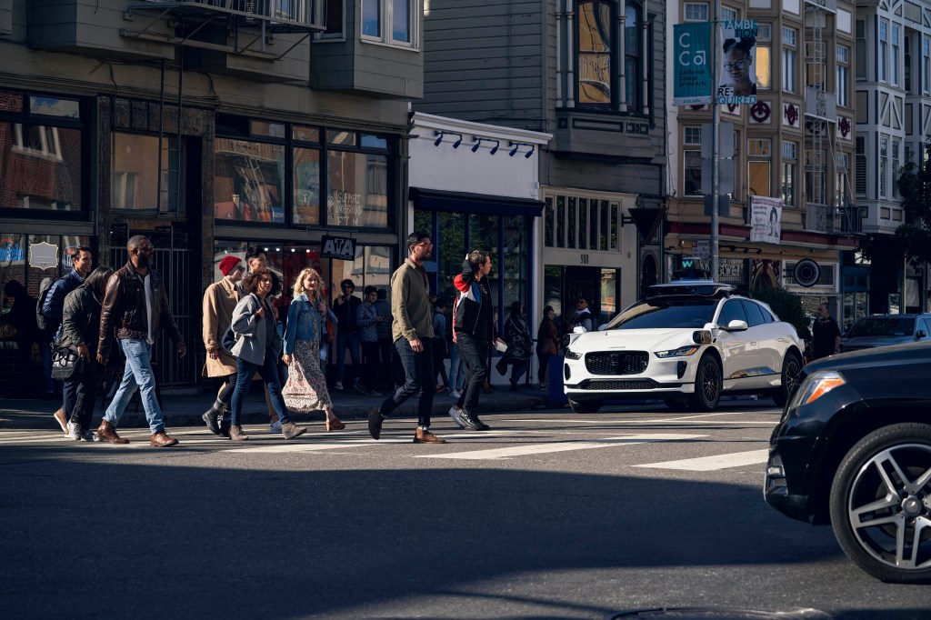 waymo jaguar i-pace at crosswalk with people walking in front