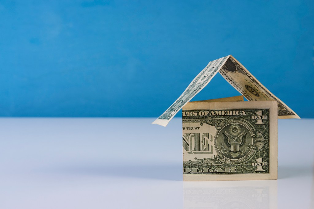 Home made from dollar notes on blue and white background, close-up. Mortgage concept