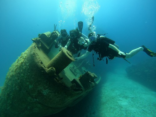 Image of three scuba divers touching a ship remain under water.