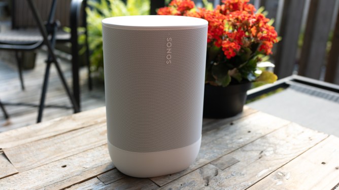 Sonos Move 2 in white on a wooden table in front of orange flowers