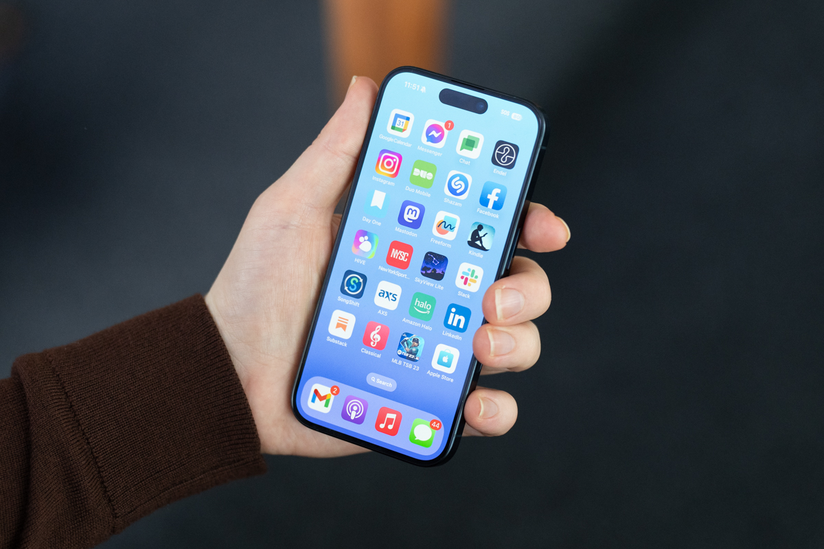 iPhone 15 Pro held in a hand, showing the front display with a Home Screen visible