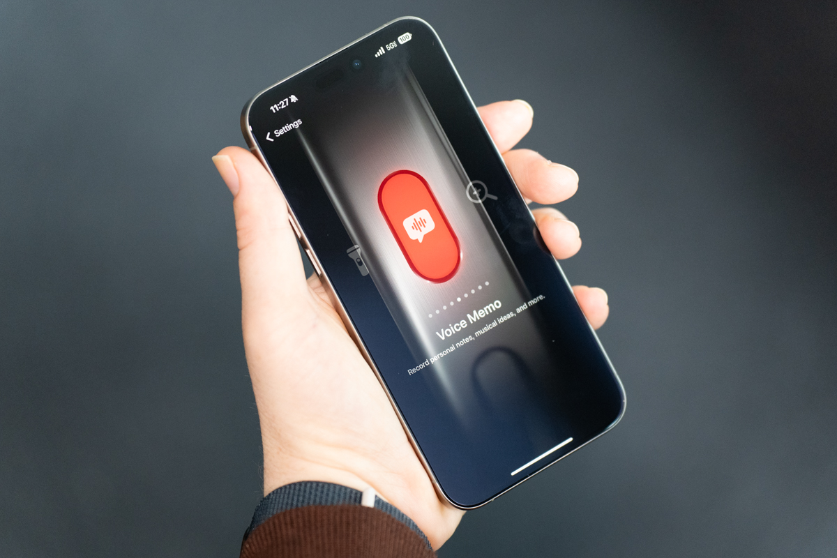 iPhone 15 Pro Max in natural titanium, being held, showing the display and Action button customization interface