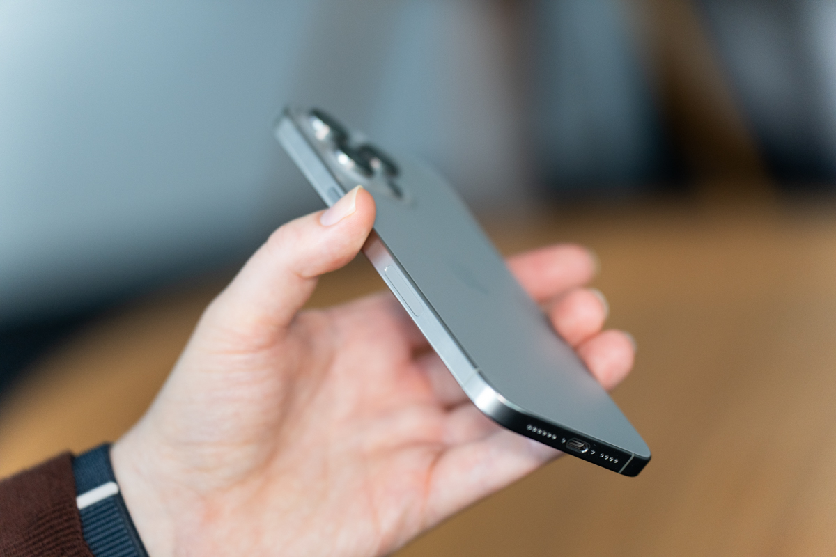 iPhone 15 Pro Max in natural titanium, being held, showing the side and back of the phone