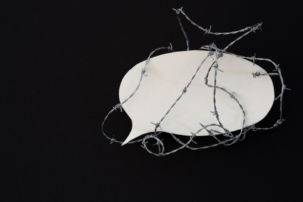 Barbed wire around a speech bubble made of paper. Black background.