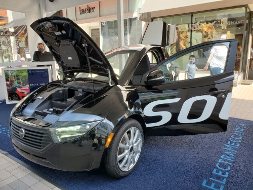 ElectraMeccanica's tiny, three-wheeled electric car is shown in black with its hood up and doors and trunk open.